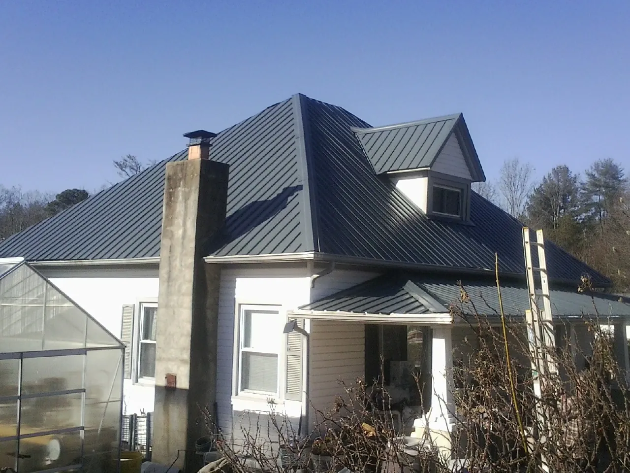 Dark blue standing seam metal roof on a white farmhouse with dormer — Slate & Tile Roof Repair by Roofing Brothers in Mc Dermott