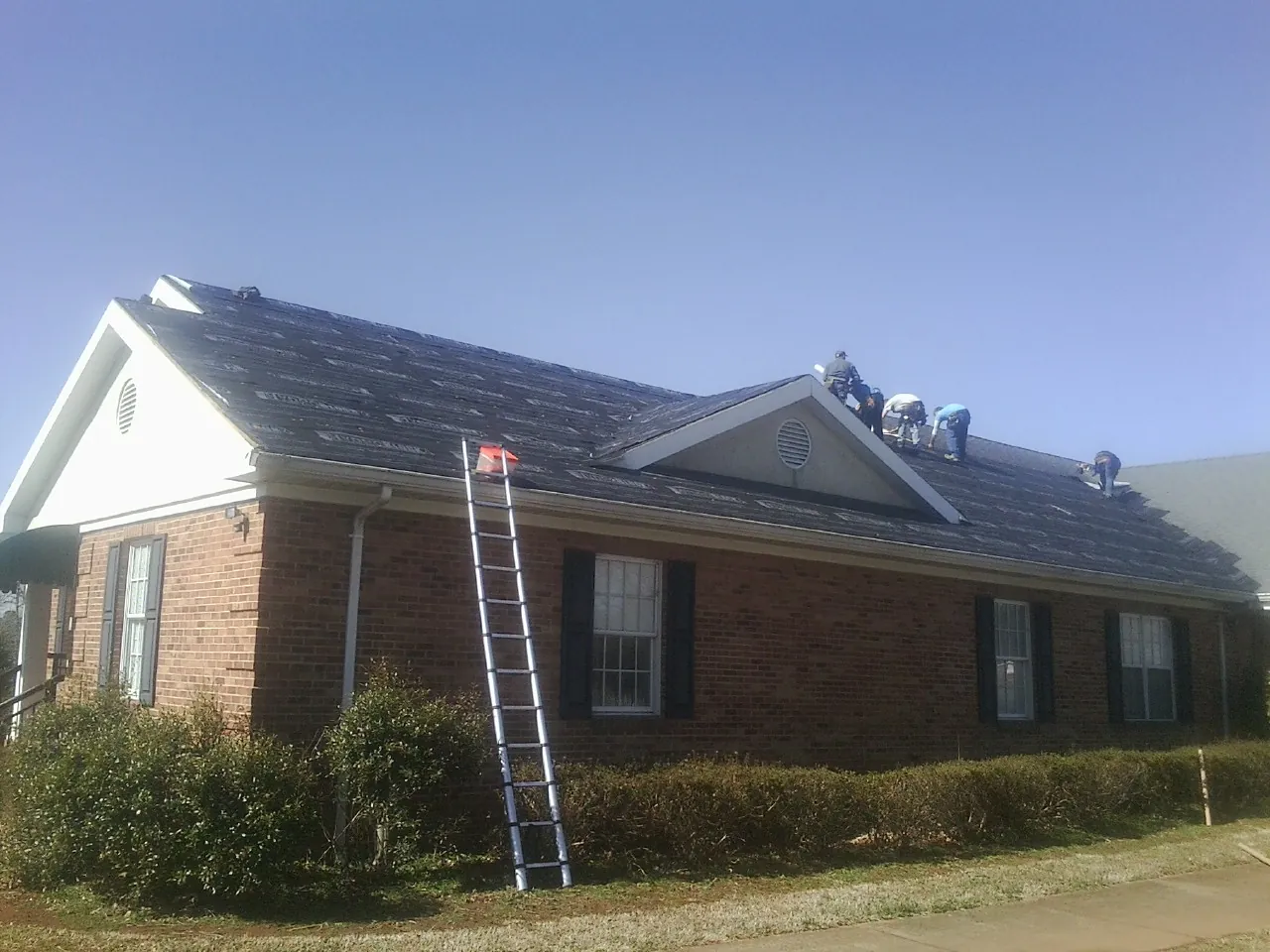 Crew tearing shingles off a brick ranch roof with a ladder set — Metal Roof Repair work by our crew in Mc Dermott