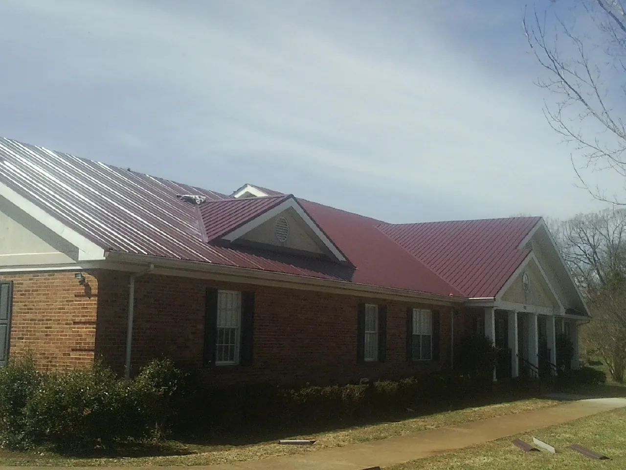 Red metal roof with gabled entries on a long brick building, from a Hail Damage Roof Repair job in Mc Dermott