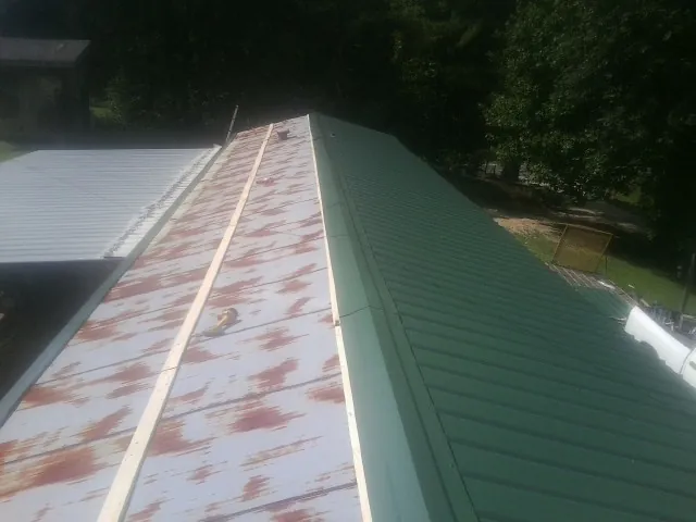 Old rusted panels beside newly installed green metal roofing — Wind Damage Roof Repair by Roofing Brothers in Mc Dermott