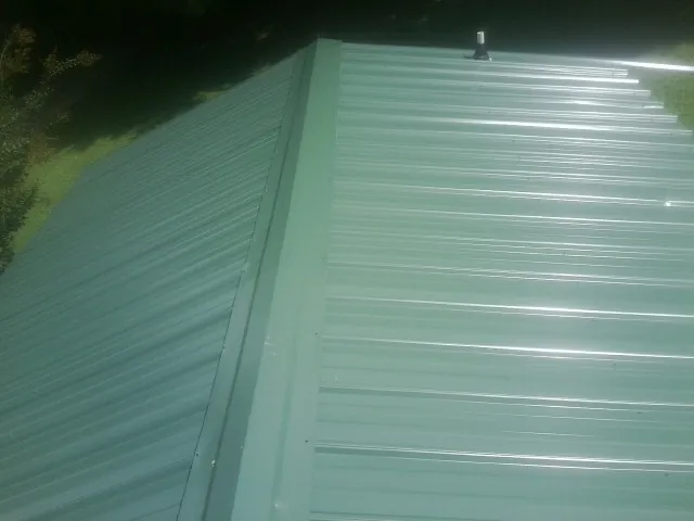 New green metal panels meeting at the ridge of a roof — Flat Roof Repair work by our crew in Mc Dermott