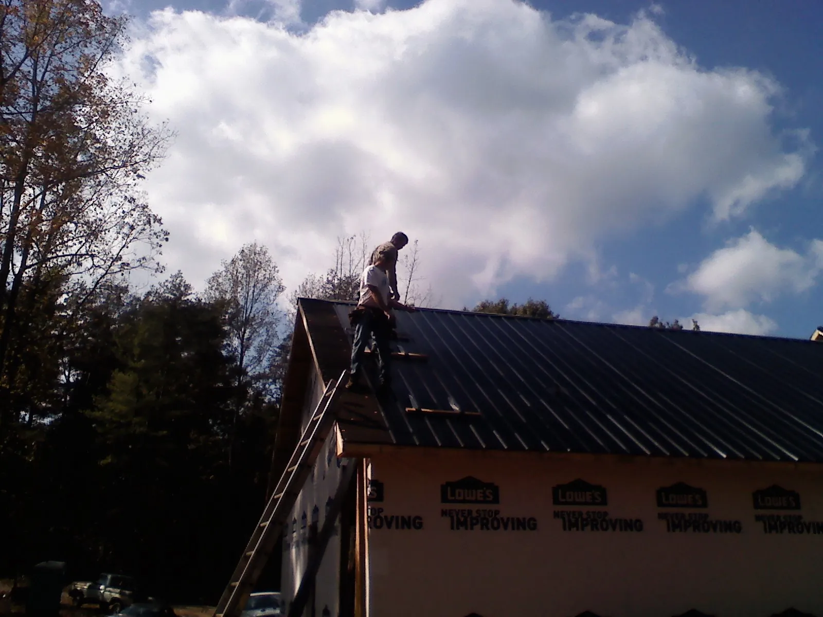Roofer fastening dark metal panels high against a cloudy sky, from a Roof Inspection job in Mc Dermott
