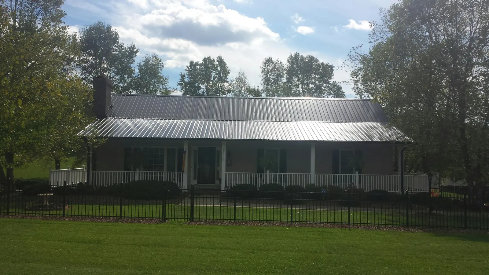 Gray metal roof on a brick ranch with a full width front porch — Gutter Guard Installation work by our crew in Mc Dermott