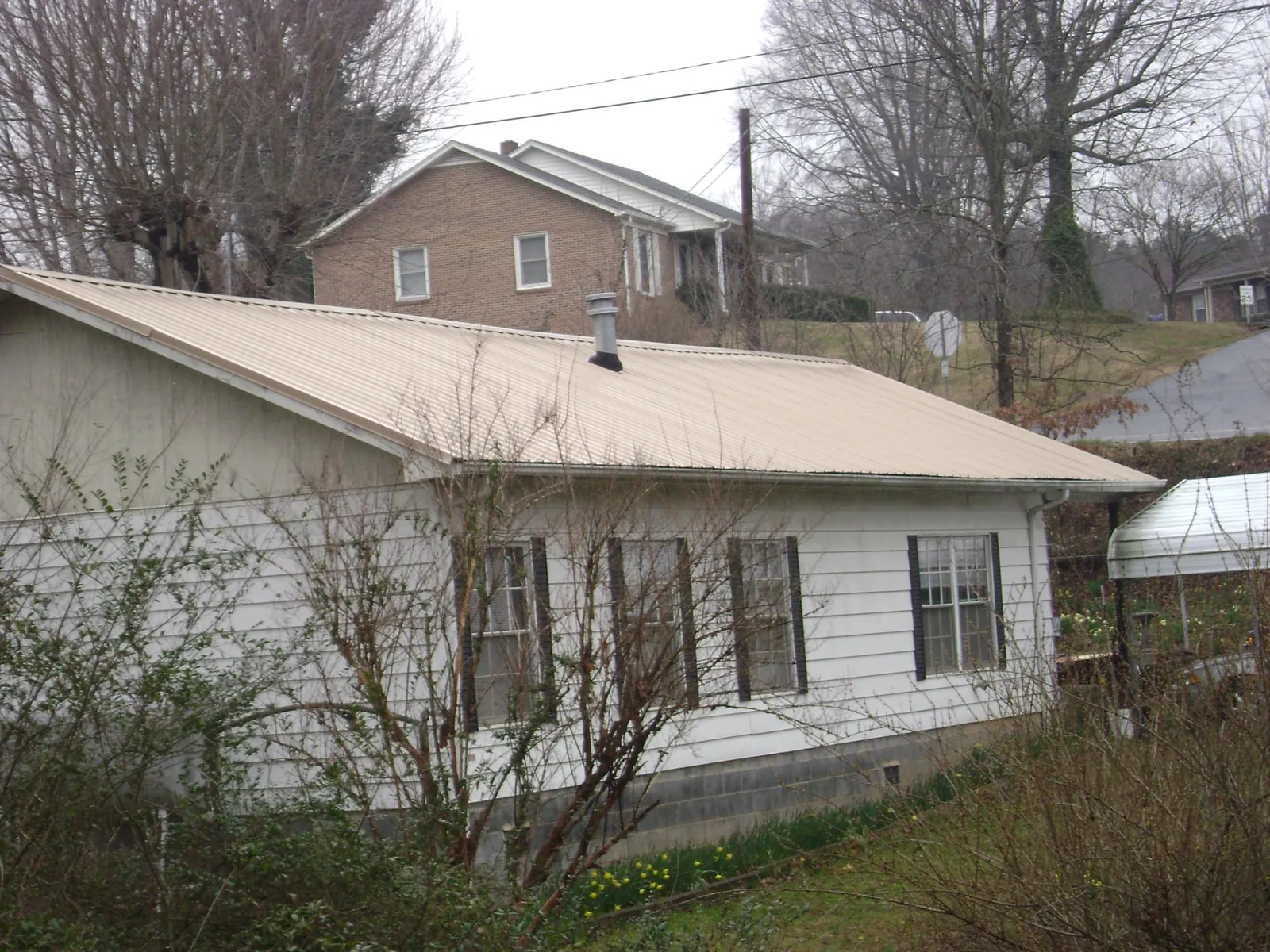 Tan metal roof on a white sided house set into a hillside — Commercial Roofing by Roofing Brothers in Mc Dermott