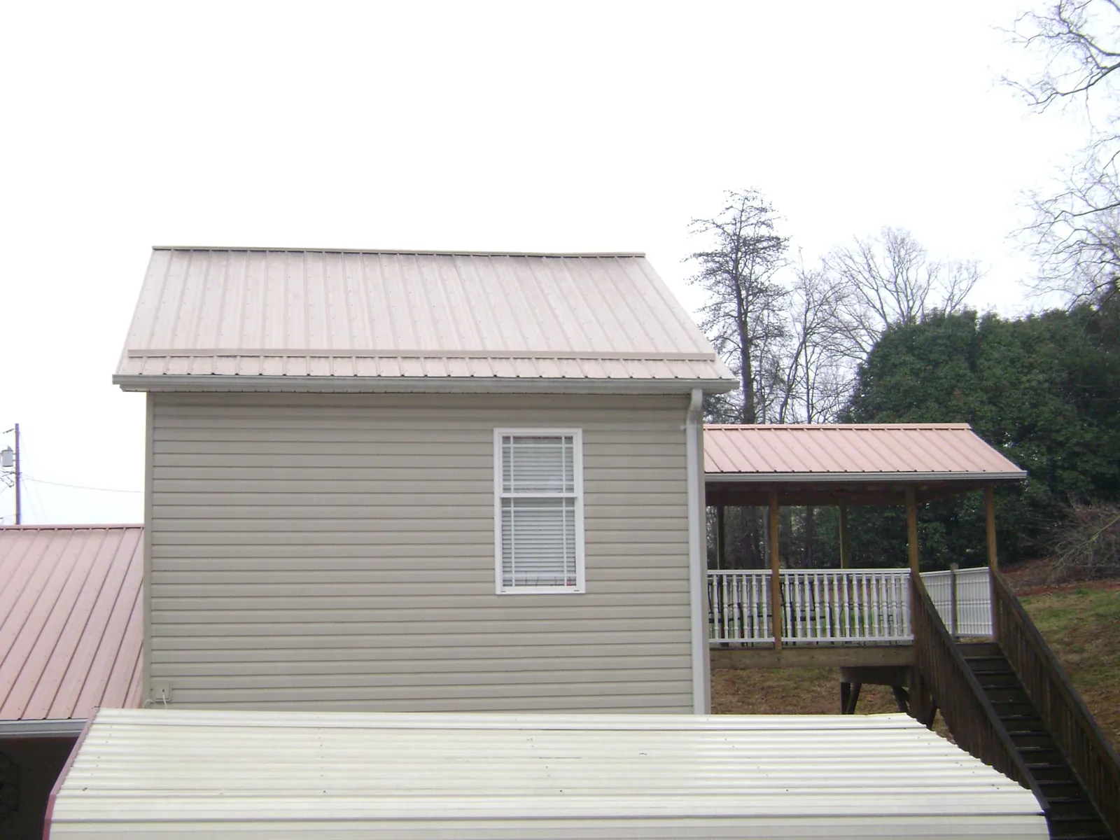 Tan metal roofs on a two story addition and attached porch, from a Roof Replacement job in Mc Dermott